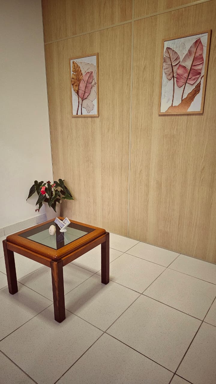 Recepção acolhedora da clínica Vital Castro, com quadros de folhas em tons rosé e uma mesinha com flores.
